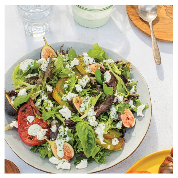 Salad with figs, tomatoes, and feta cheese on a white table.